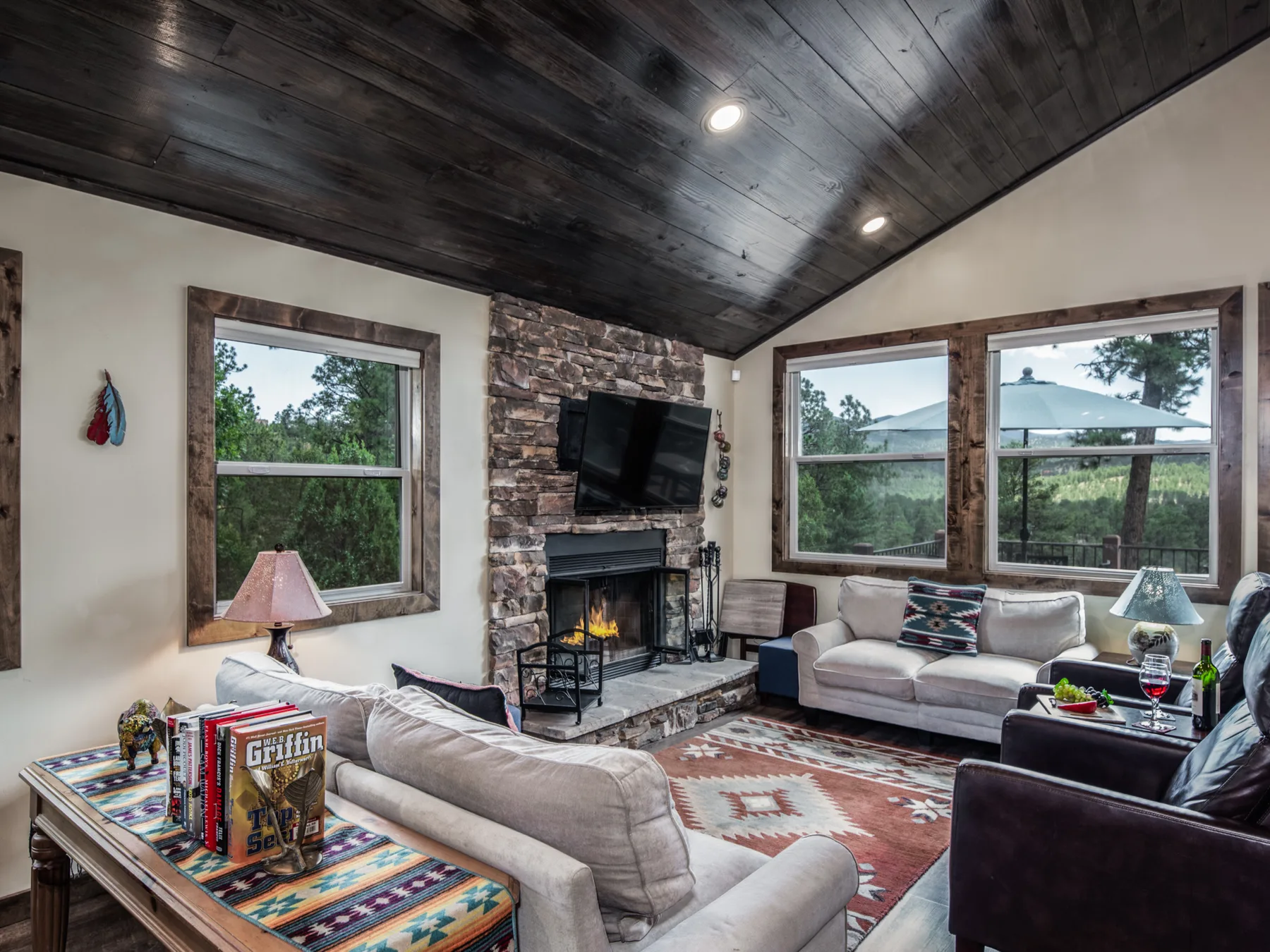A living room with a stone fireplace, television, and seating beneath a dark wood ceiling.