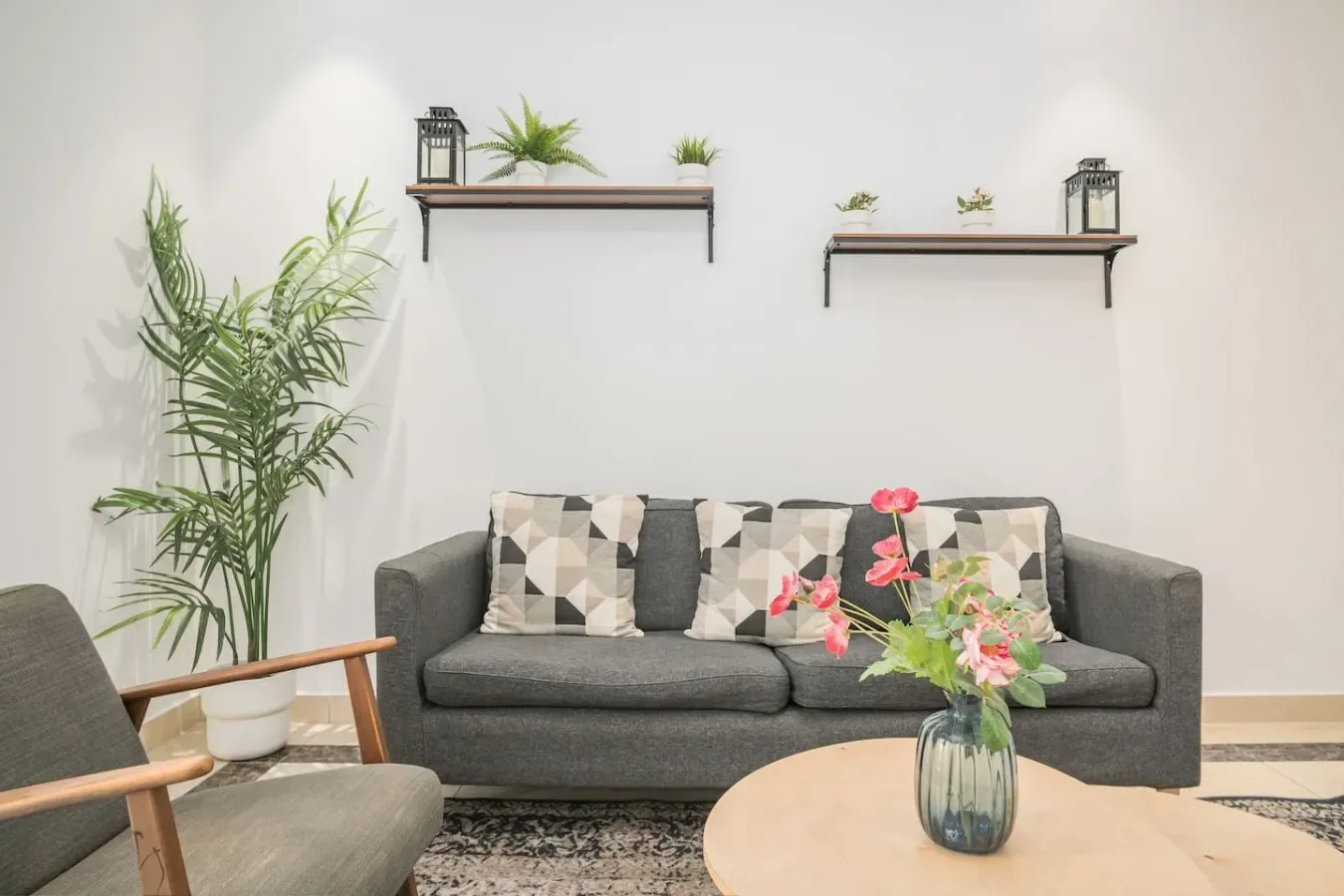 Una sala de estar con un sofá gris, plantas y una mesa de centro baja.