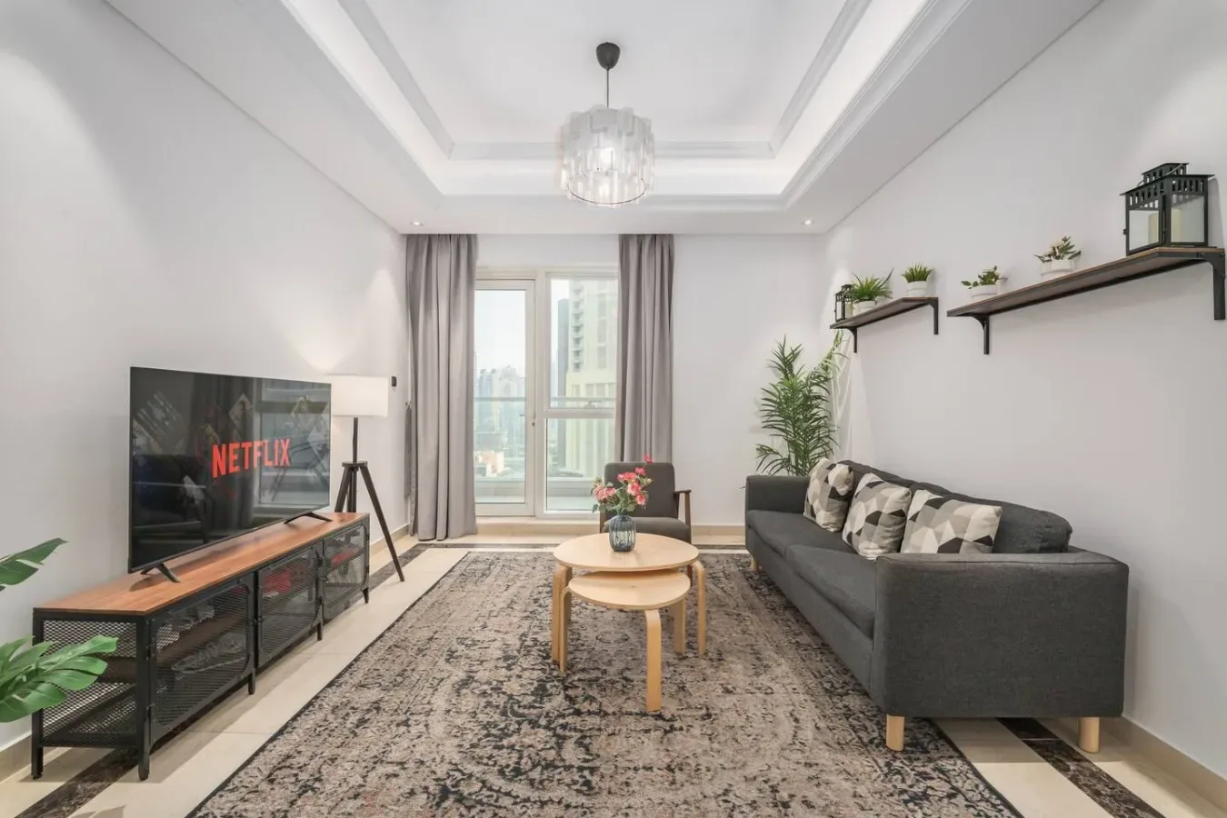 Una sala luminosa con sofá gris, televisor y ventanales.