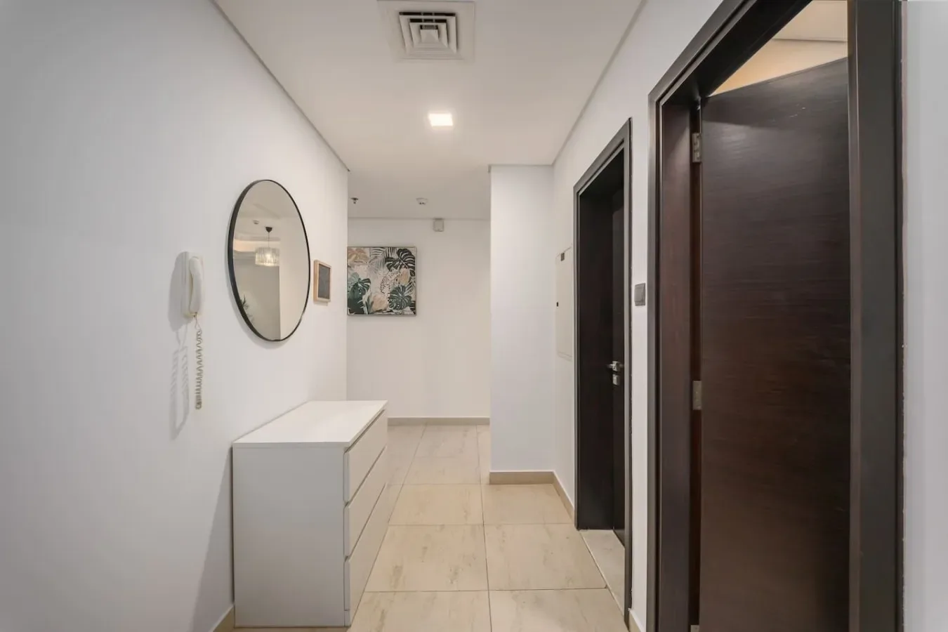Un pasillo luminoso con una cómoda blanca y puertas oscuras.