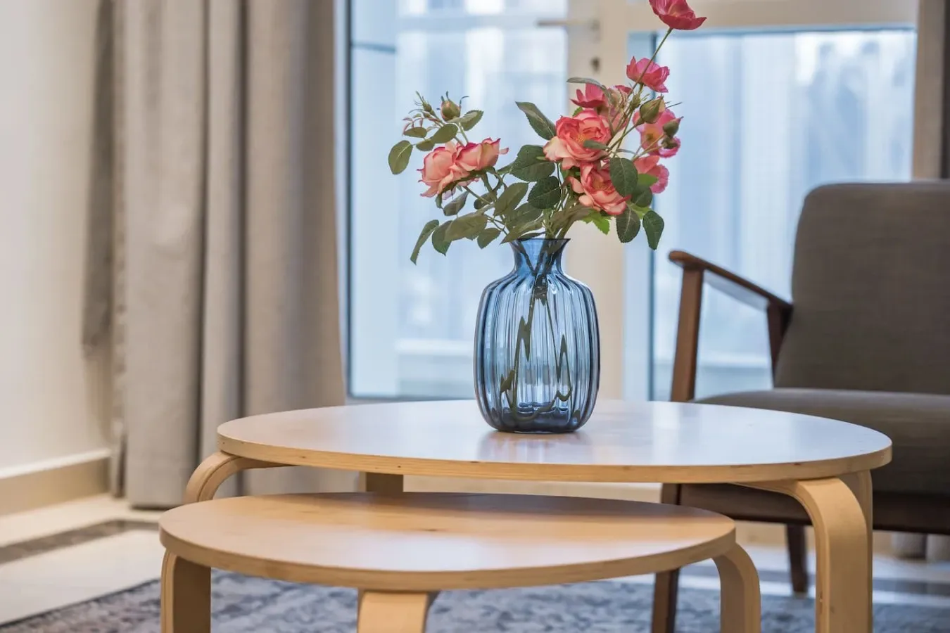 Una zona de estar con una mesa redonda, un banco de madera y flores junto a una ventana.
