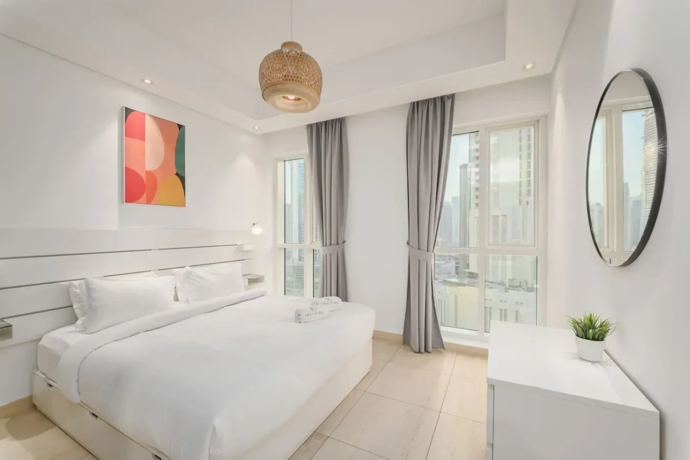 Un dormitorio luminoso con ropa de cama blanca, cortinas grises y ventanas grandes.