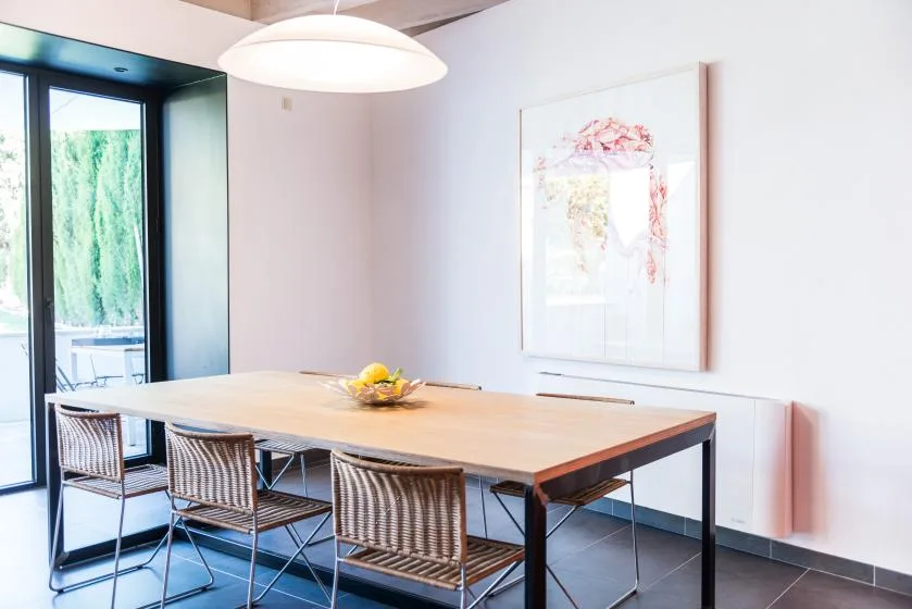 Comedor con una mesa larga y asientos tejidos junto a una ventana grande.