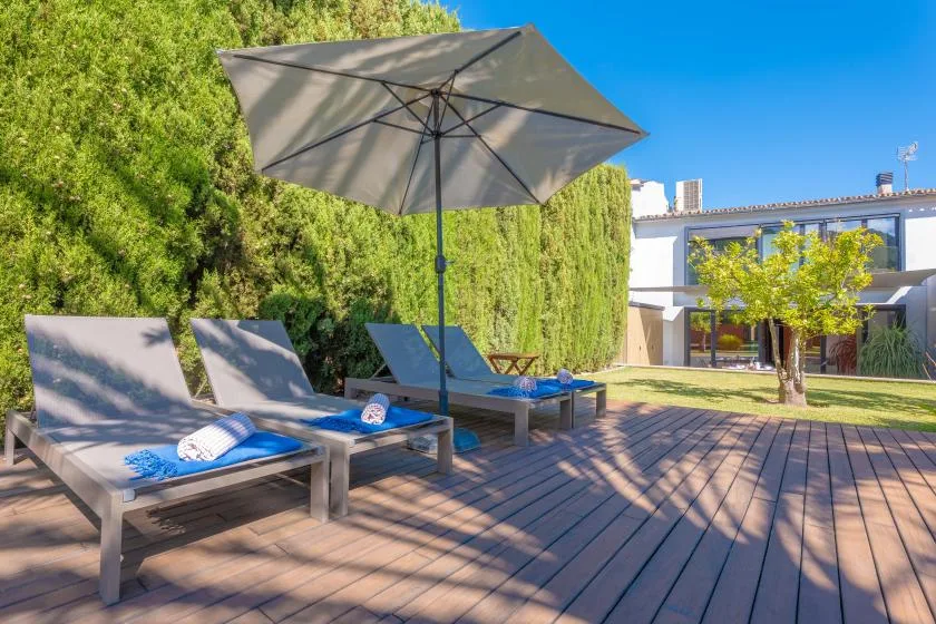 Una terraza exterior con asientos acolchados bajo una sombrilla grande.