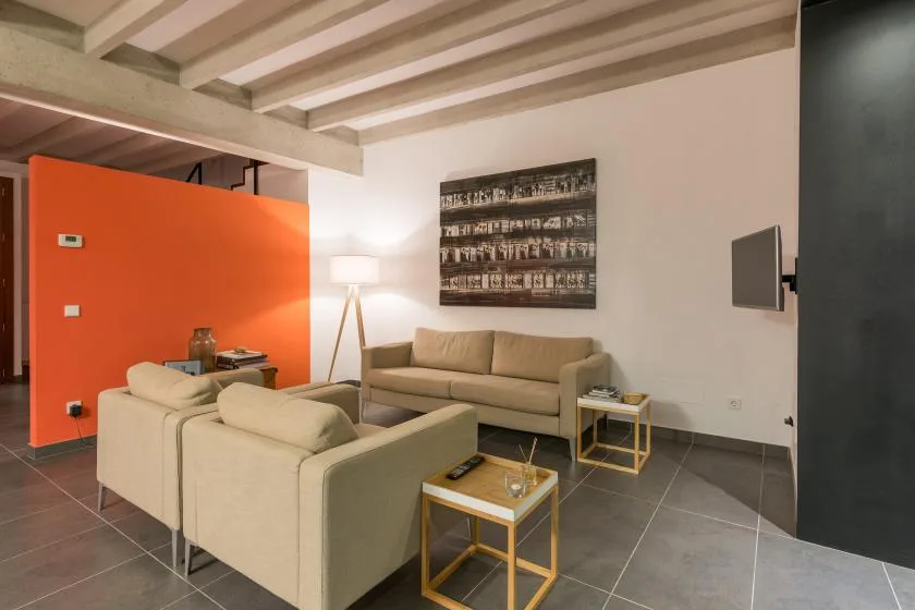 Una sala de estar moderna con asientos beige, mesas de centro y una pared naranja.