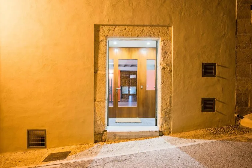 Una entrada iluminada se abre desde una pared exterior amarilla hacia un pasillo interior.