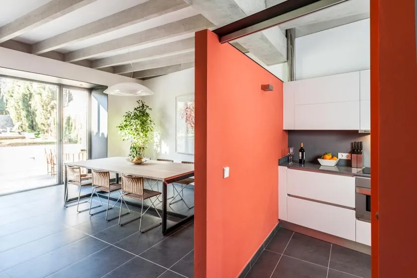 Comedor abierto junto a una cocina, con una mesa cerca de grandes puertas de vidrio.