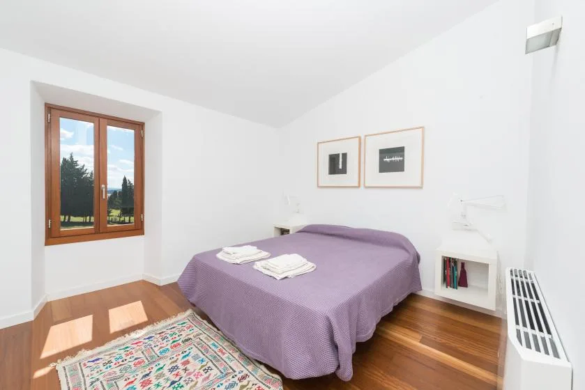 Un dormitorio luminoso con una cama morada, una ventana y una alfombra estampada.