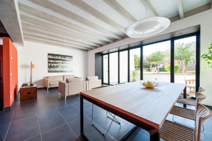 Una luminosa zona de comedor y estar con una mesa larga junto a grandes puertas de vidrio.