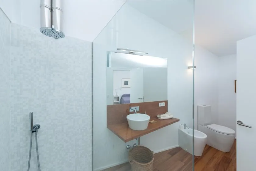 Un baño luminoso con ducha de vidrio, lavabo e inodoro.