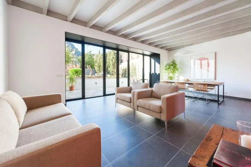 Una luminosa sala de estar con asientos junto a grandes puertas de vidrio y vegetación al exterior.
