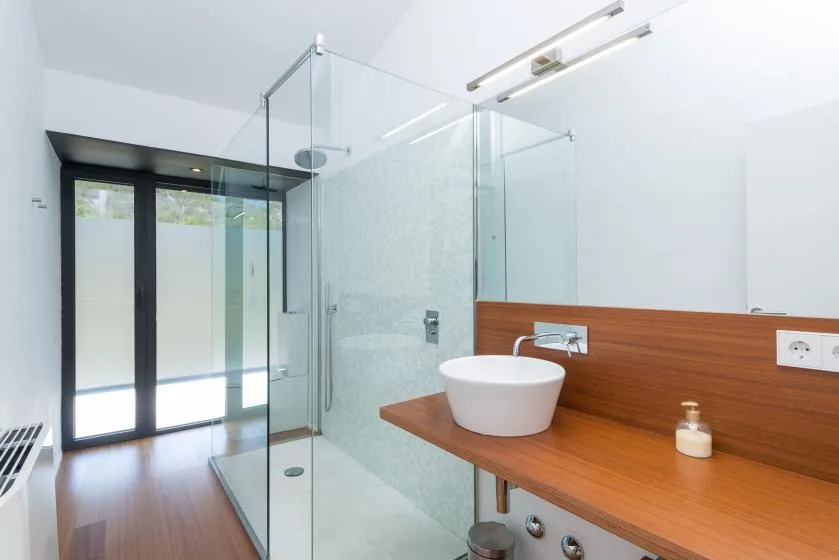 Un baño luminoso con ducha de vidrio y lavabo sobre una encimera de madera.