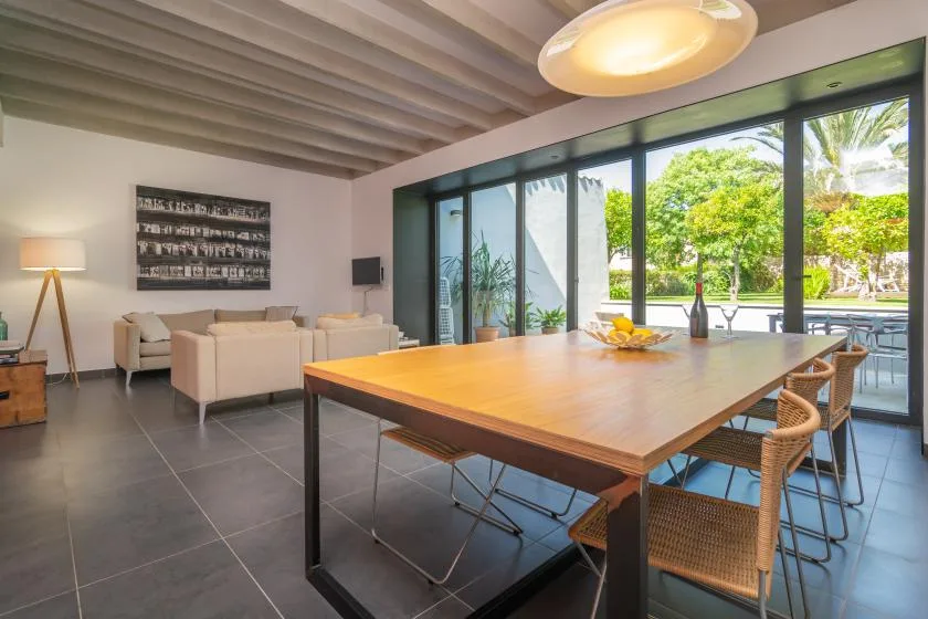 Un comedor con una gran mesa de madera junto a amplias puertas de vidrio que dan a un jardín.