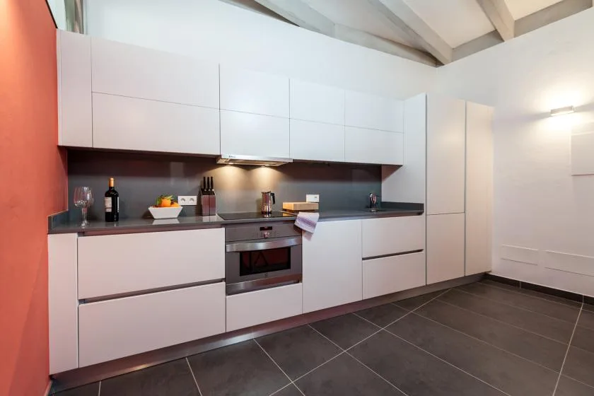 Una cocina moderna con gabinetes blancos, una encimera oscura y un horno integrado.