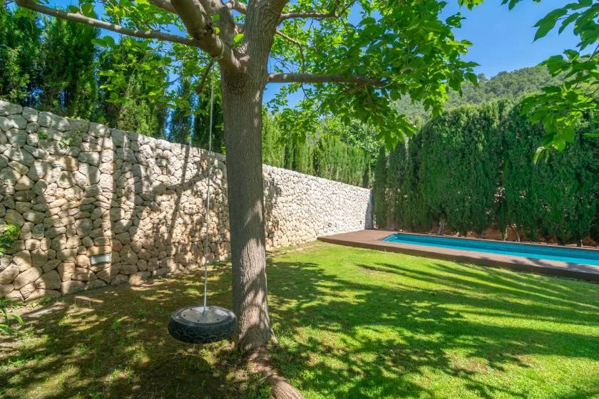 Un jardín frondoso con un muro de piedra y una piscina.