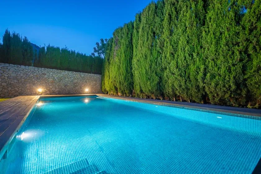 Una piscina al aire libre está rodeada de altos setos verdes y un muro de piedra.
