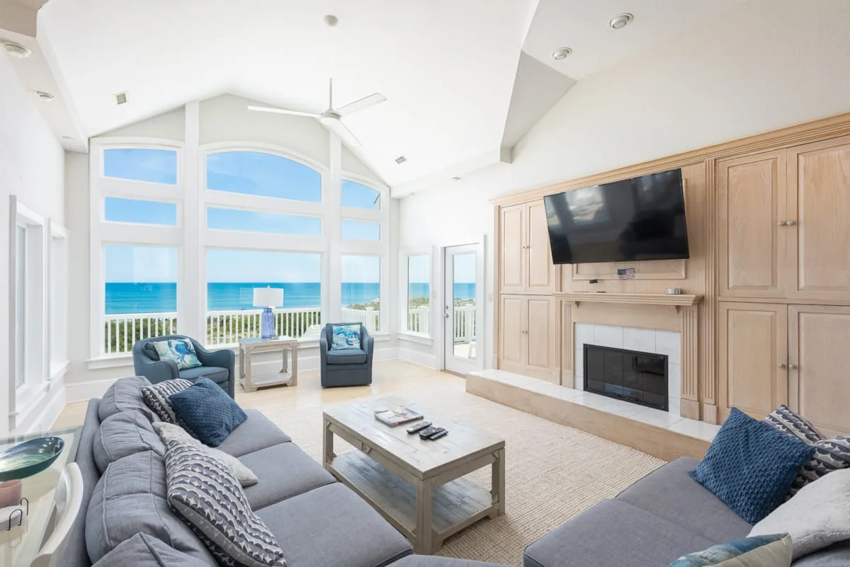 Una sala luminosa con asientos, un televisor en la pared y vistas al mar por grandes ventanas.