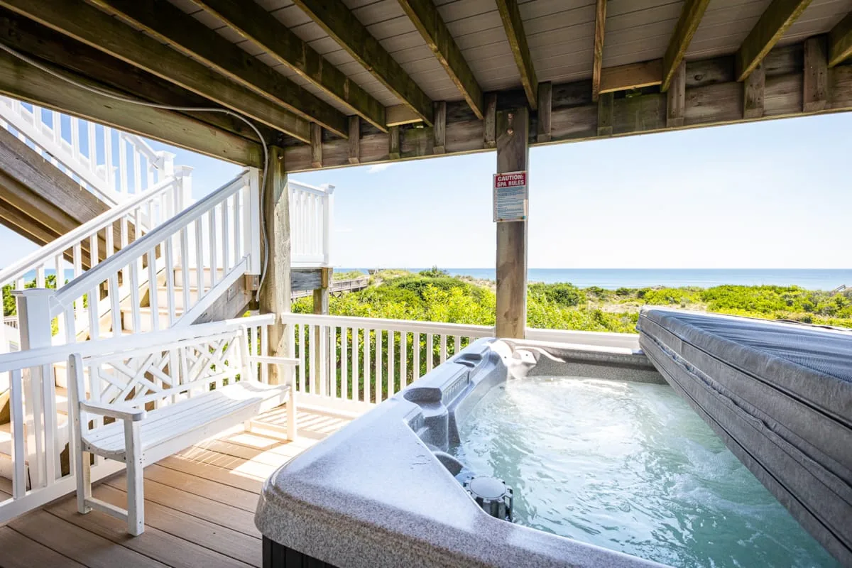 A covered outdoor hot tub overlooks green vegetation and the ocean.