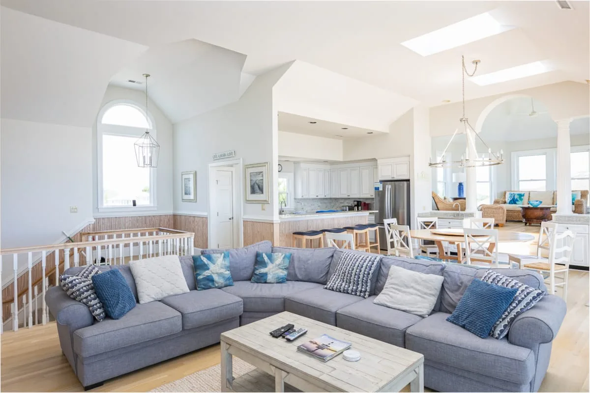 A bright open-plan living room with a gray sectional and kitchen beyond.