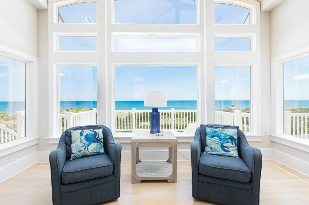 A bright sitting area with two armchairs facing large windows overlooking the ocean.
