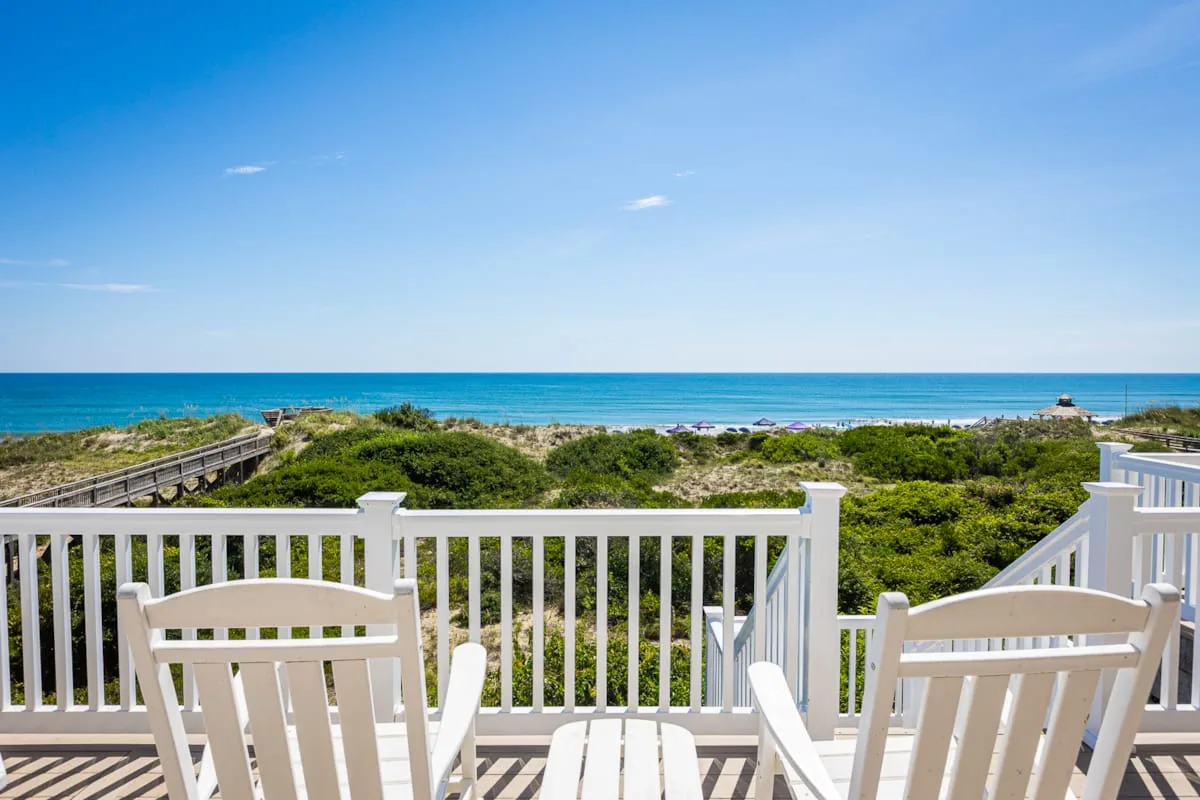 A seaside deck with white seating overlooks coastal greenery and the ocean.