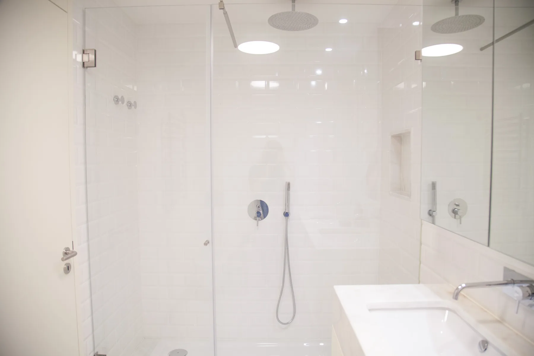 A bright white-tiled bathroom with a shower and sink.