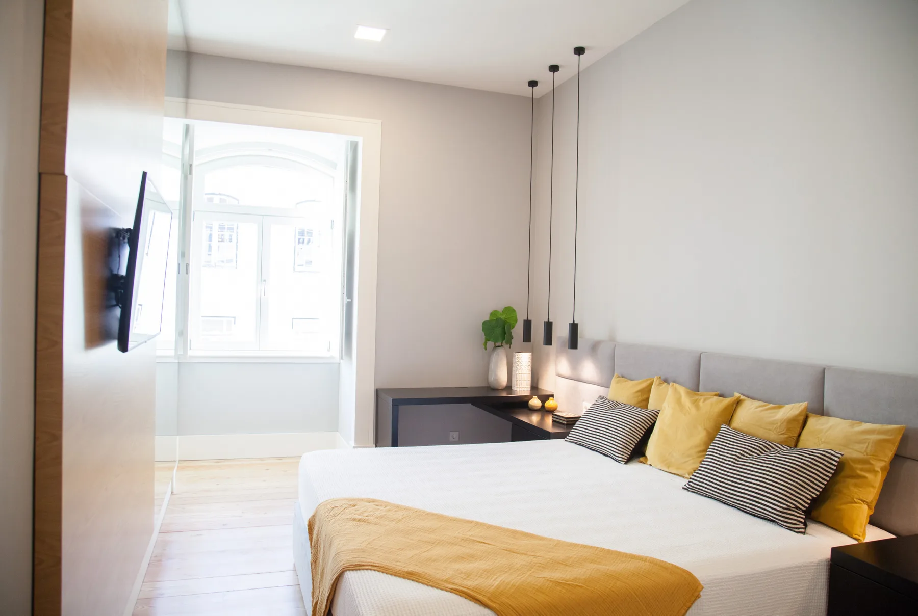 A bedroom with a bed, yellow cushions, and a television mounted on the wall.