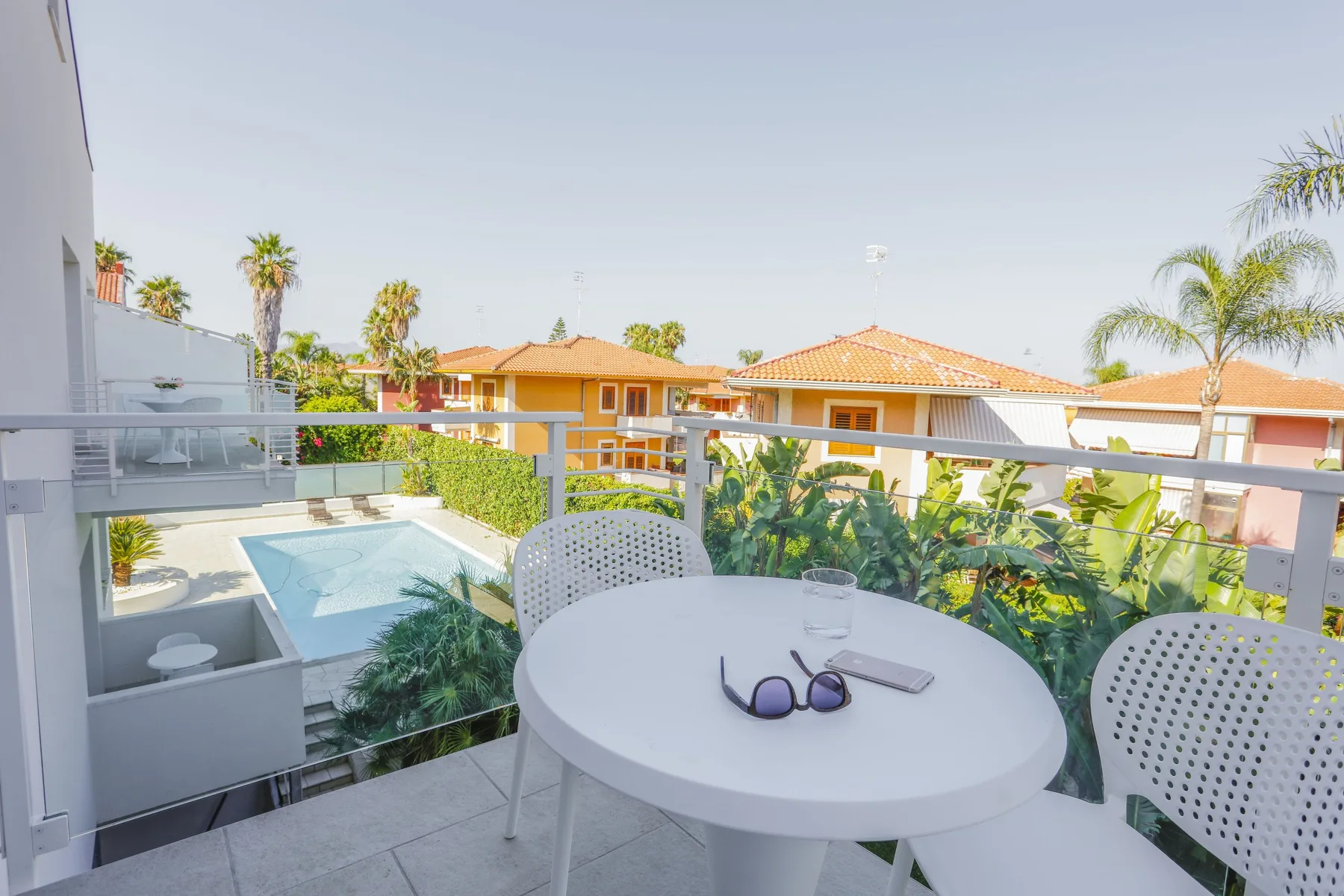 Una zona de estar en el balcón da a una piscina y casas cercanas.