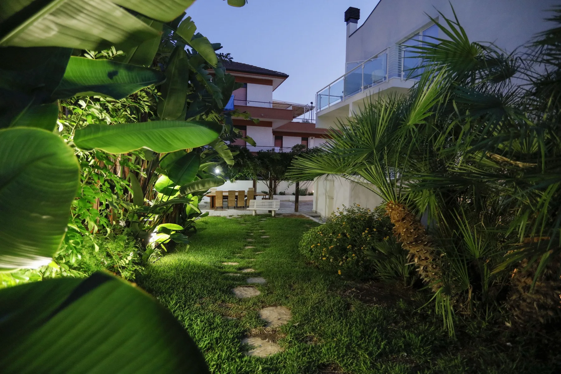 Un sendero de jardín atraviesa una vegetación frondosa junto a un edificio moderno.