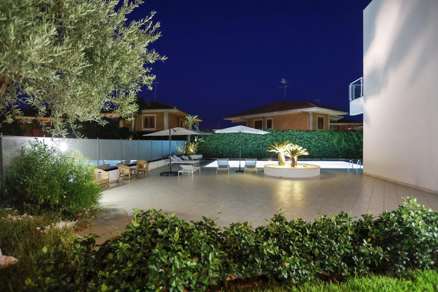 Un patio exterior junto a una piscina, con asientos y un elemento de jardín iluminado.