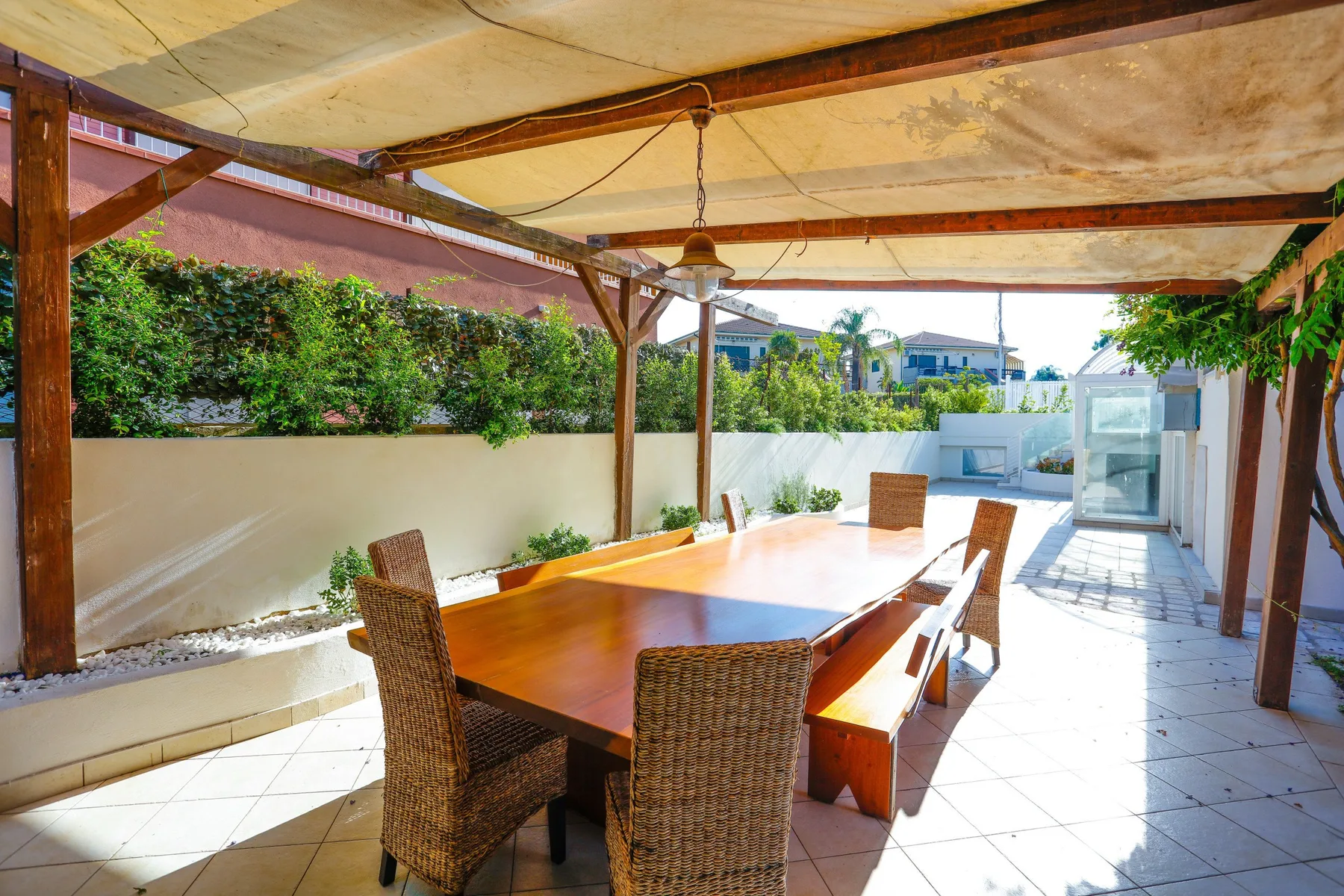 Comedor exterior a la sombra con una mesa larga y asientos de mimbre.