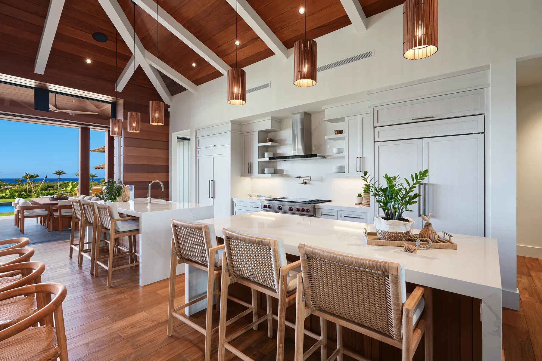 Una luminosa cocina y comedor con una barra larga, asientos tejidos y vistas al mar.