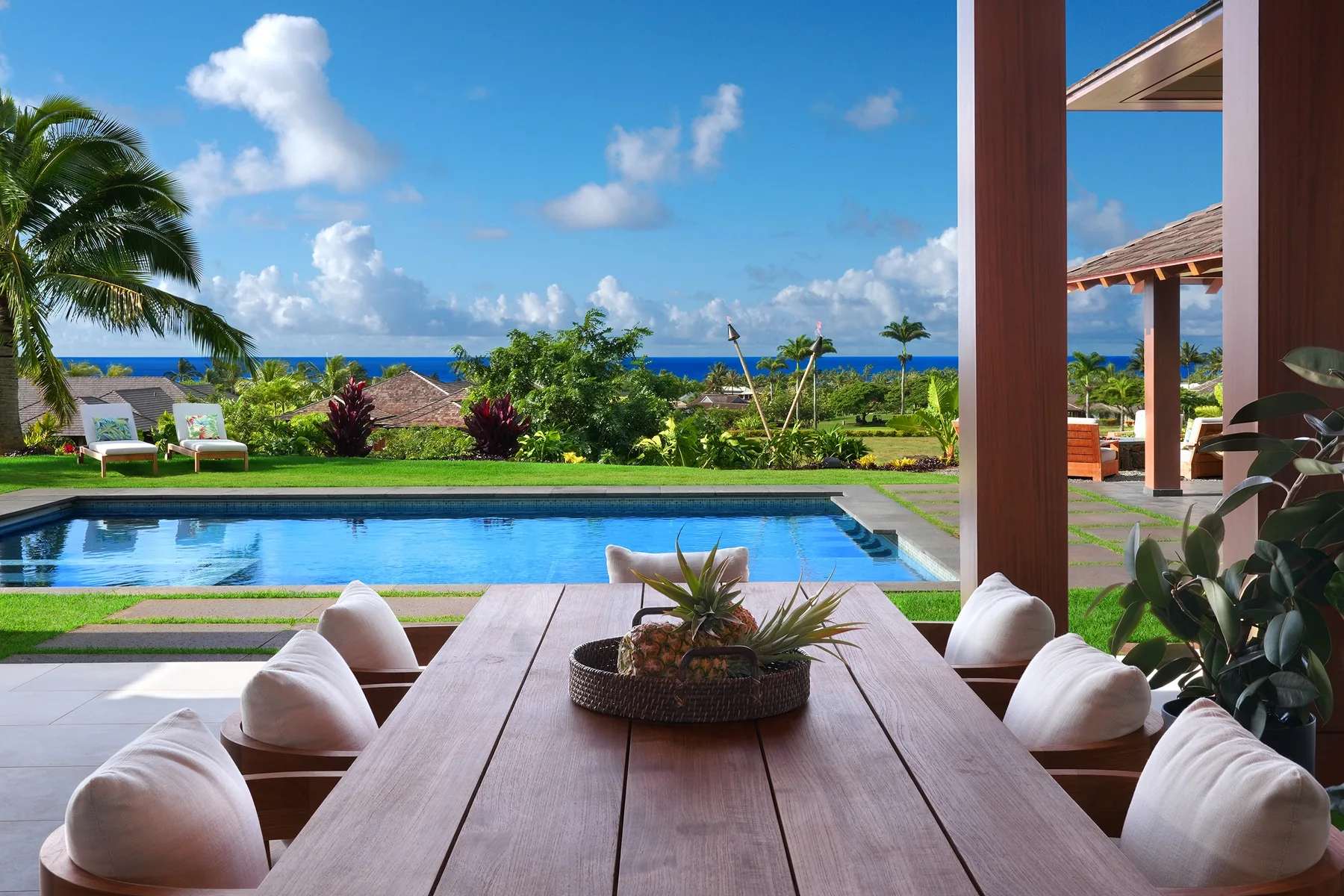 Una mesa de comedor al aire libre da a una piscina, un jardín y el mar.