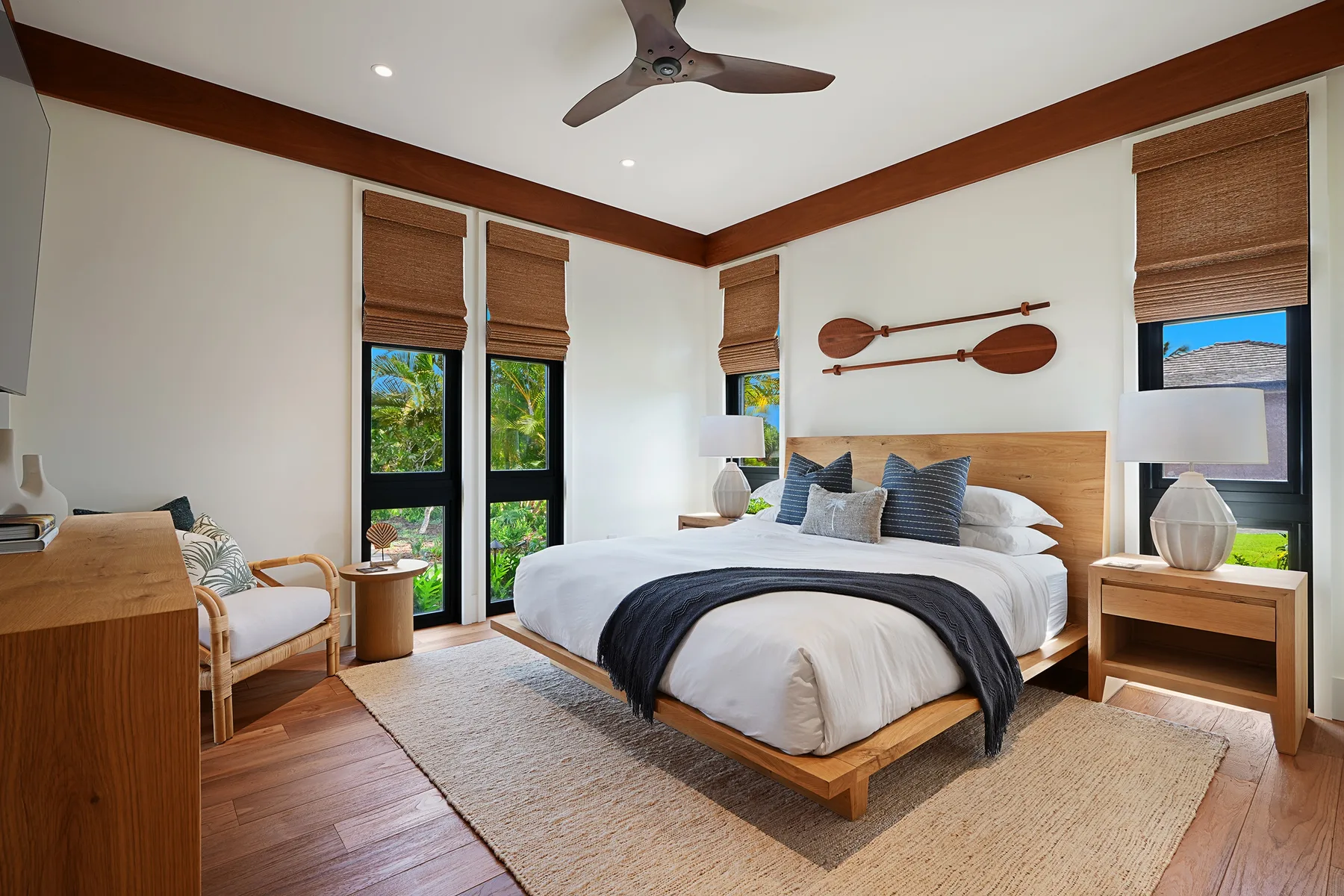 Un dormitorio luminoso con una cama grande, muebles de madera y ventanas altas.