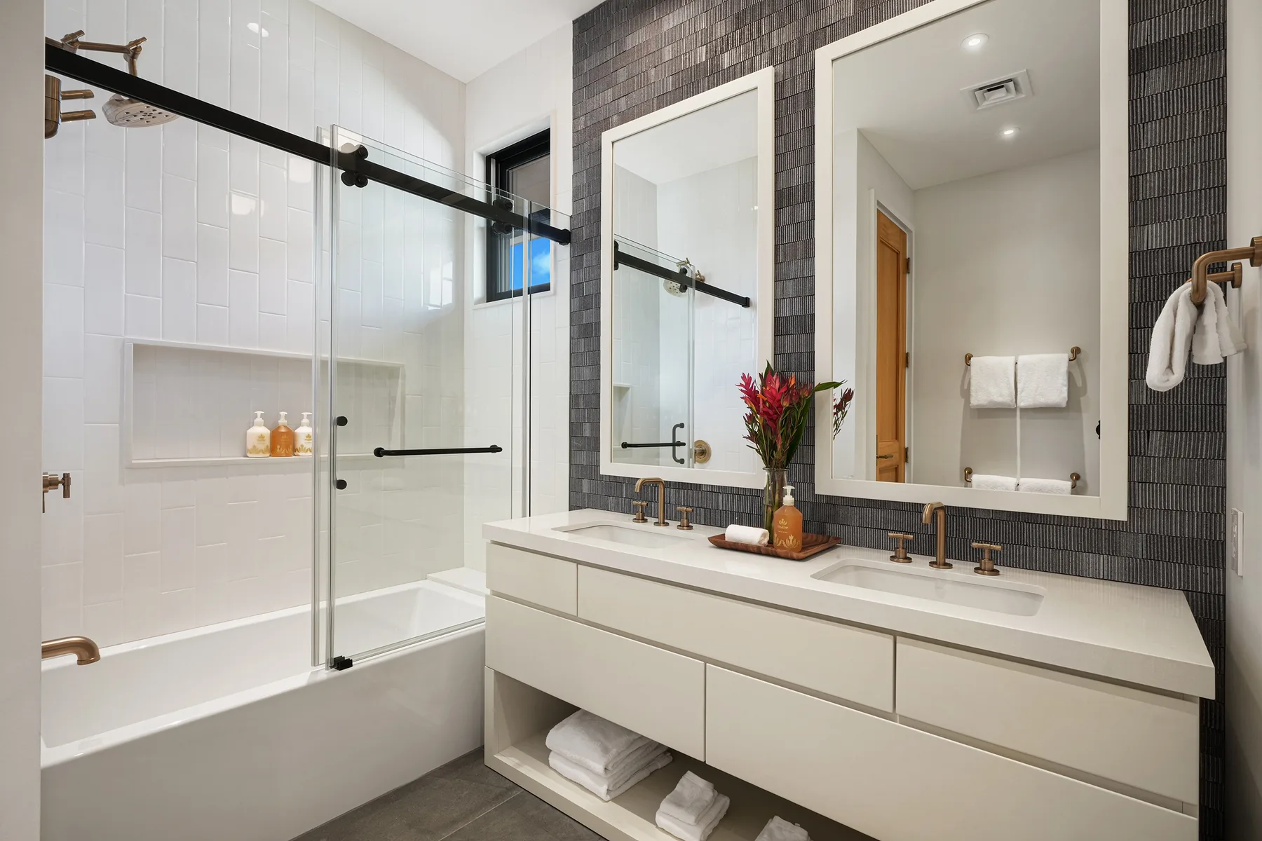 Un baño luminoso con bañera, mampara de vidrio y tocador doble.