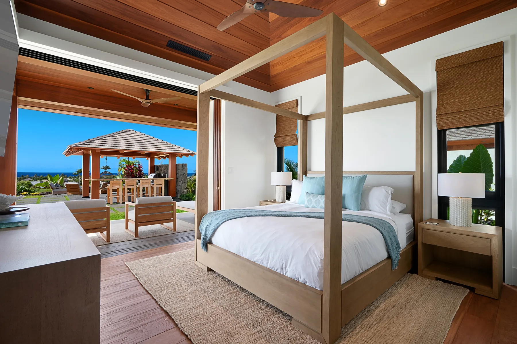 Un dormitorio con cama de dosel de madera se abre a un patio amueblado con vistas al mar.