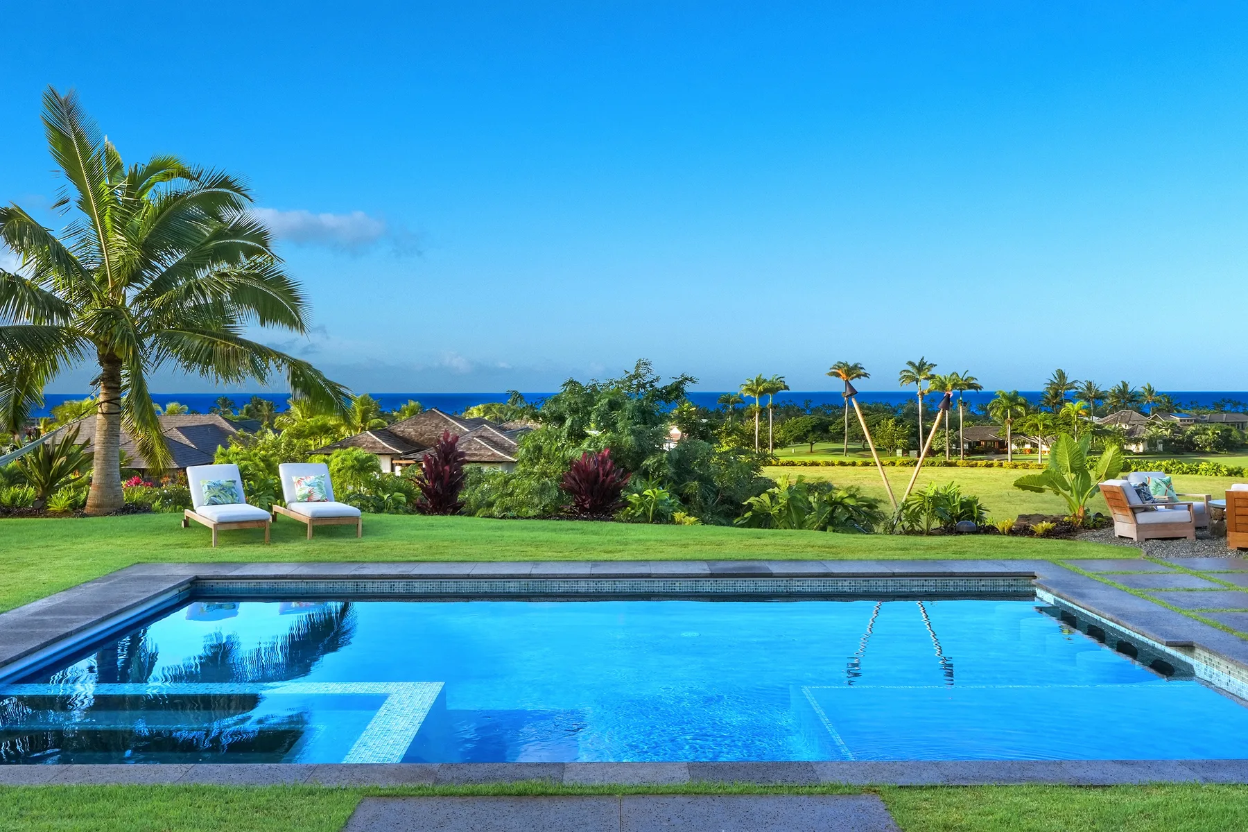 Una piscina al aire libre da a un jardín paisajístico y al mar.
