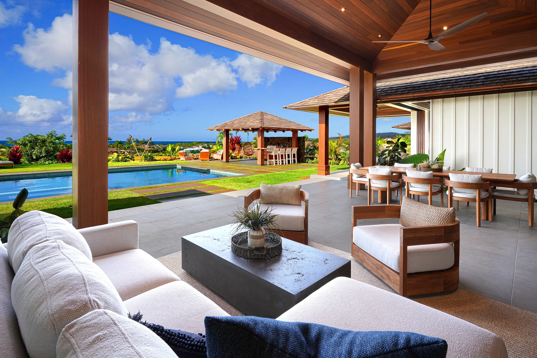 Un patio cubierto tiene asientos y una mesa de comedor junto a una piscina.