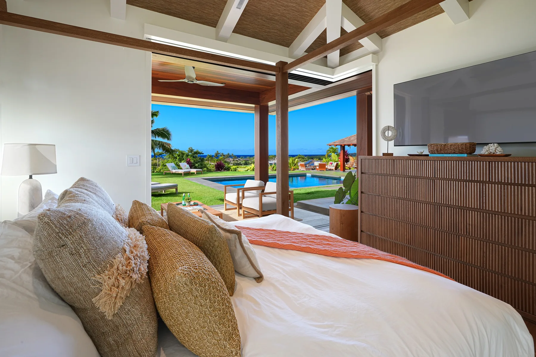 Un dormitorio se abre a una terraza y una piscina, con el mar visible más allá del jardín.