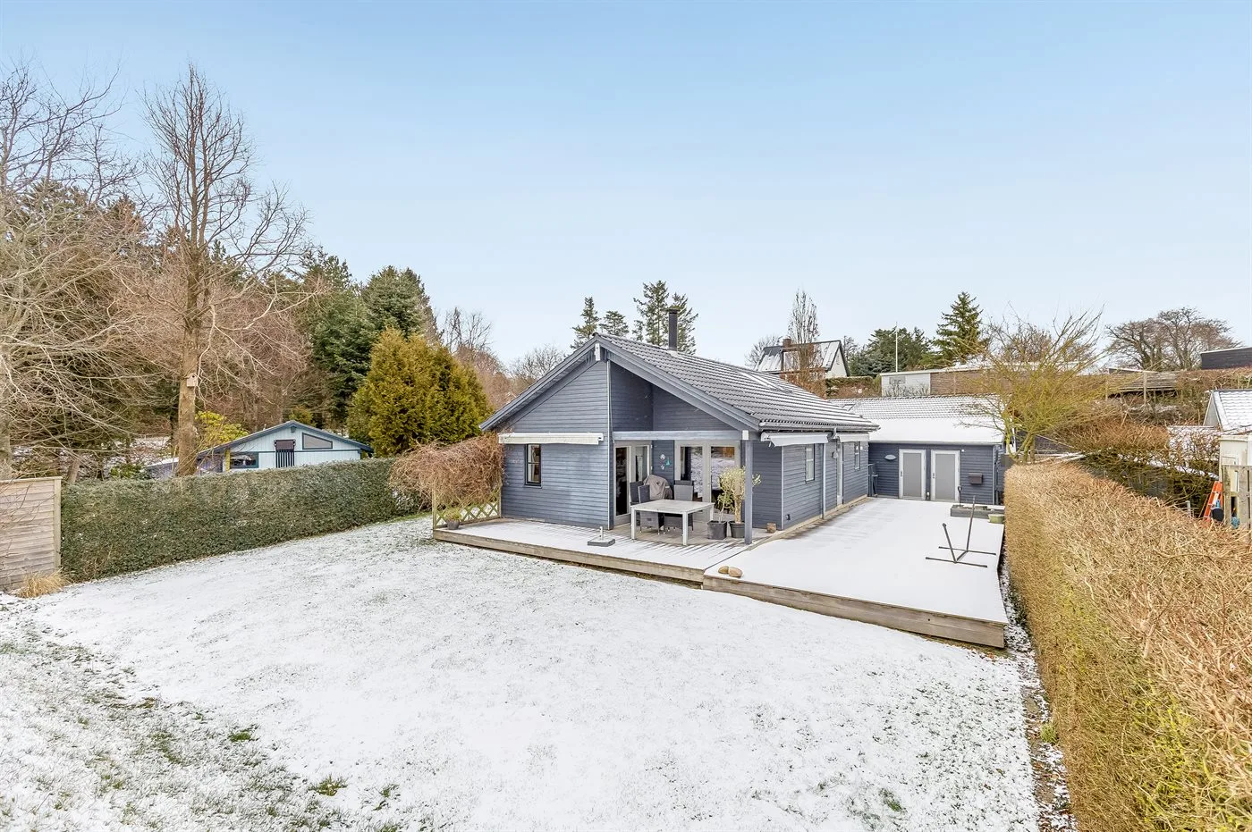 Una casa moderna junto a un patio y un jardín cubierto de nieve.