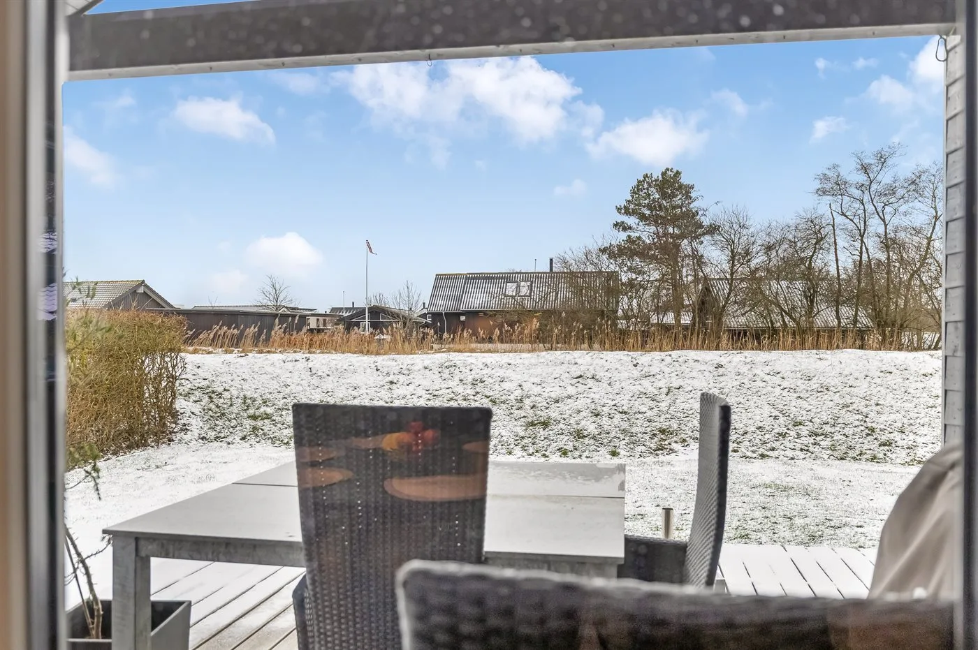 Un patio nevado con asientos al aire libre da a un campo abierto.