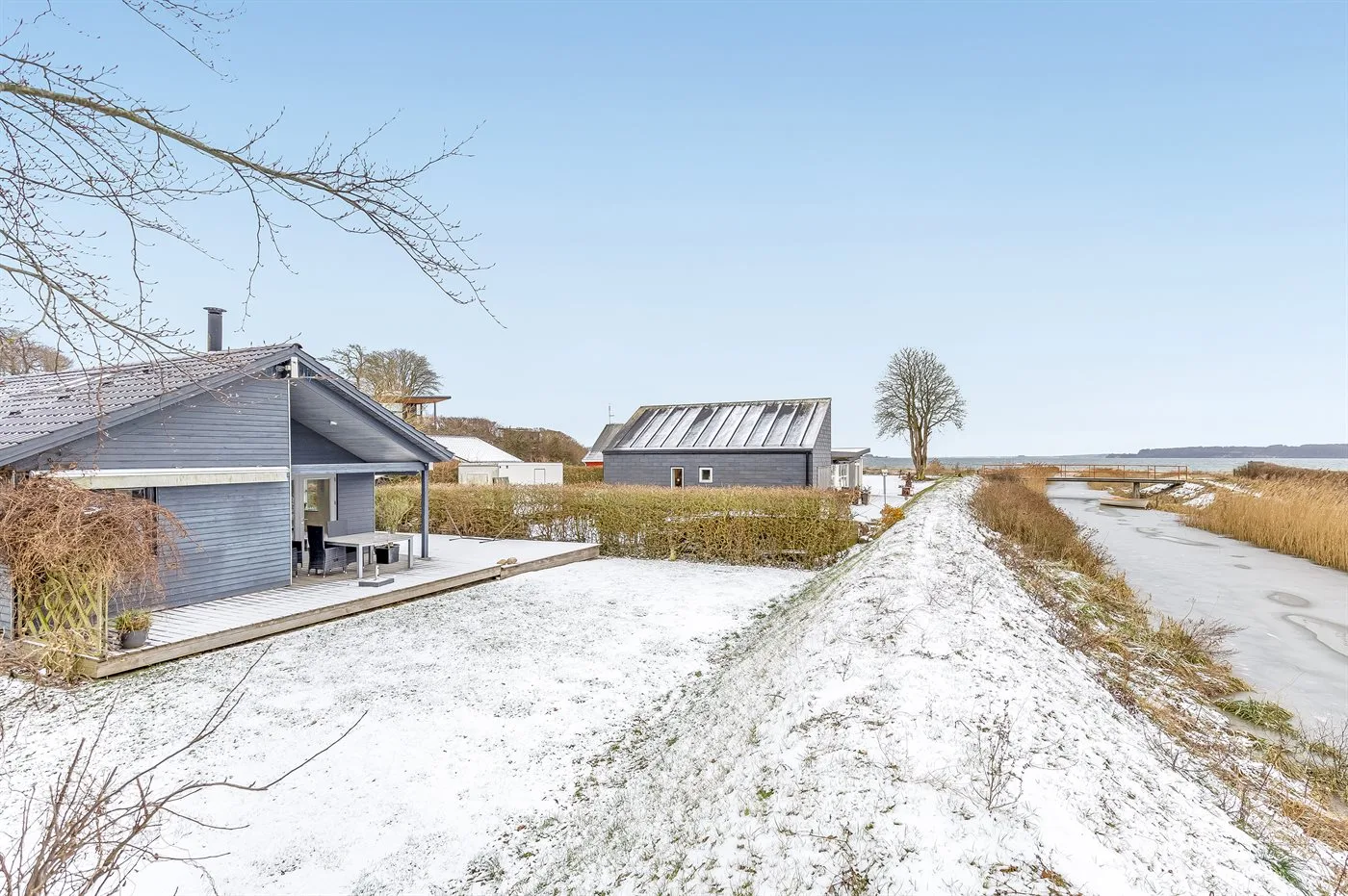 Camino cubierto de nieve entre una casa moderna y un pequeño edificio junto a un canal.