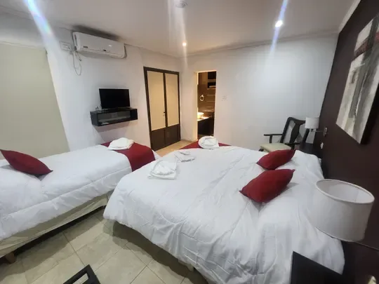 Cama doble y cama individual con cojines rojos, un televisor y aire acondicionado.
