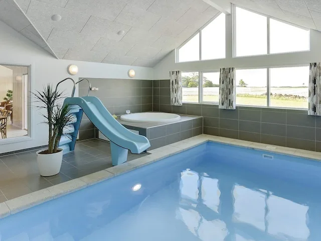 An indoor pool area with a blue slide and a raised hot tub.