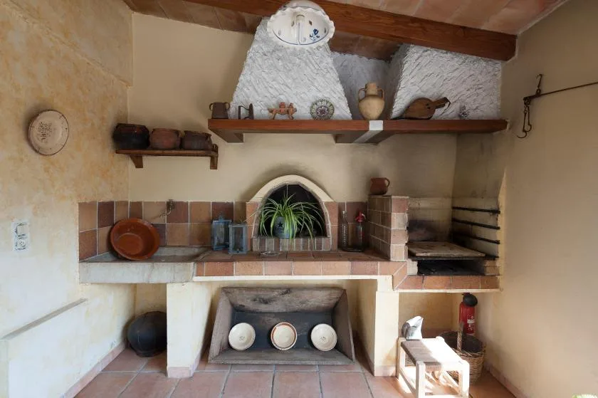A rustic indoor hearth with a small arched opening and tiled surround.