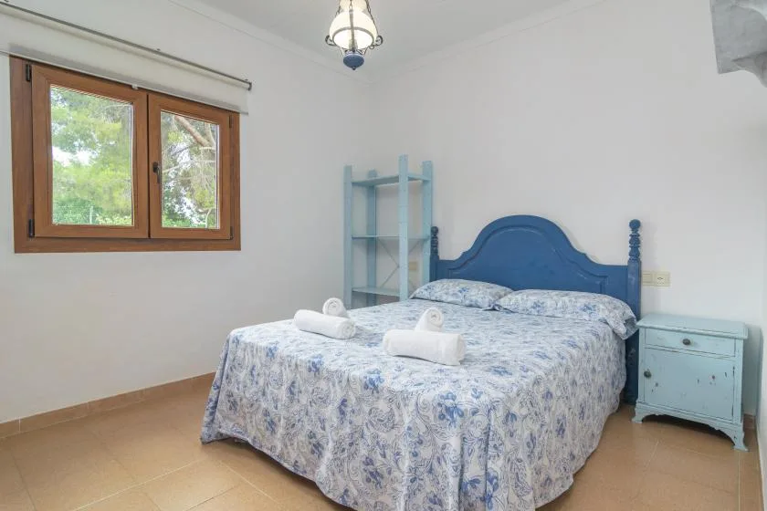 A bedroom with a blue bed, a window, and a small bedside table.