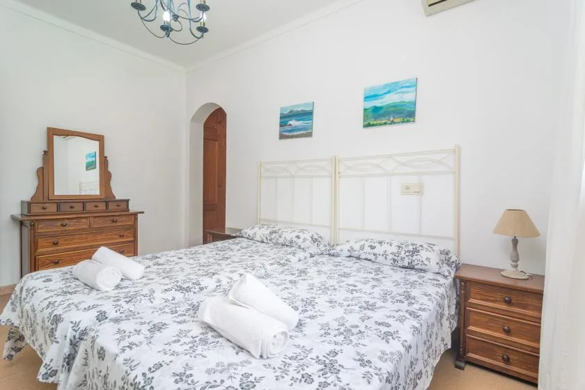 A bright bedroom with floral bedding, white towels, and wooden furniture.