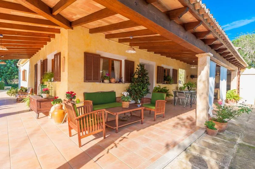 Un patio cubierto con asientos de madera, plantas en macetas y un largo suelo de baldosas.