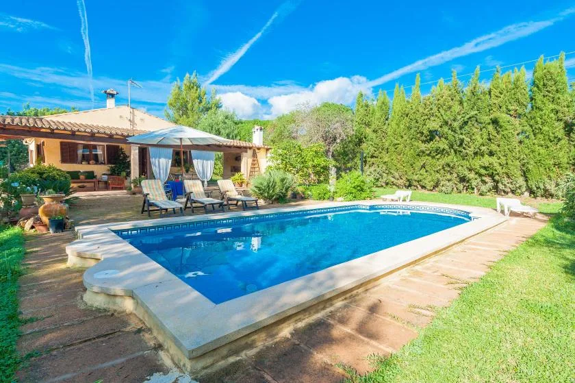Una piscina está junto a un patio con asientos al aire libre y un jardín.