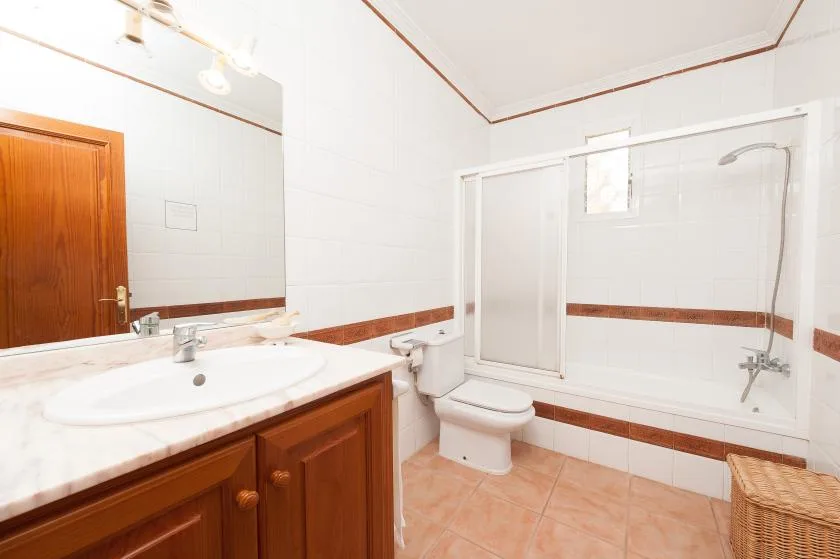 A bathroom with a vanity, toilet, and bathtub-shower behind a glass screen.